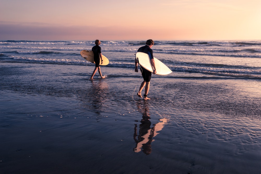 two people surfing in Oahu during sunset